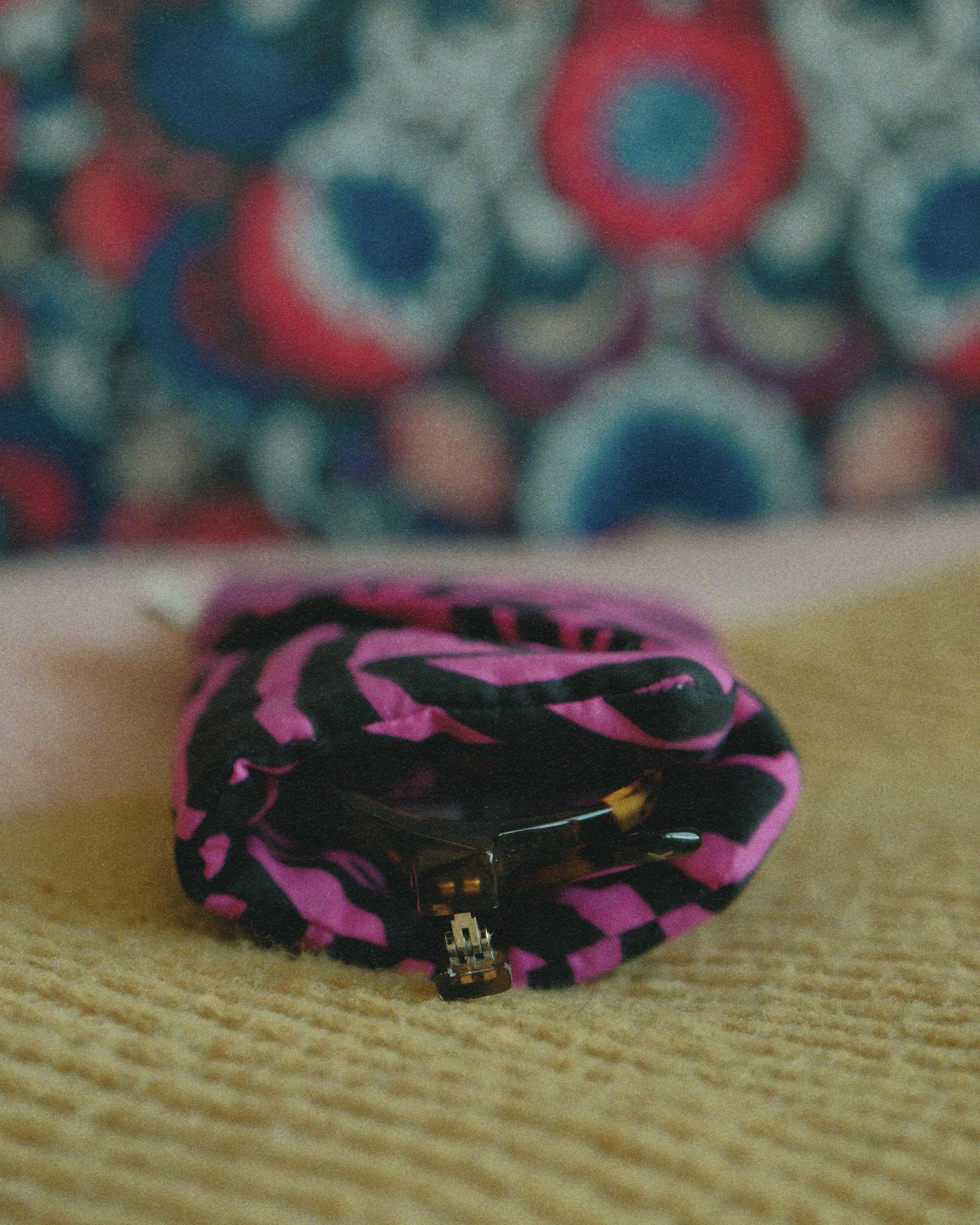 Pink and black patterned pouch on a textured surface with a colorful abstract background